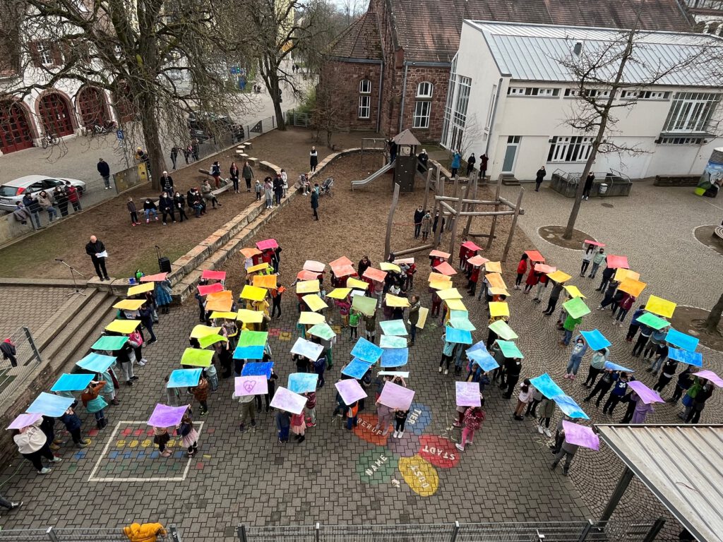 Gruppe von Kinder halt farbige Plakate über ihre Köpfe sodass ein Regenbogen entsteht