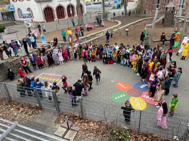Foto verkleideter Grundschulkinder die auf einem Schulhof im großem Halbkreis stehen um eine Vorführung anzusehen