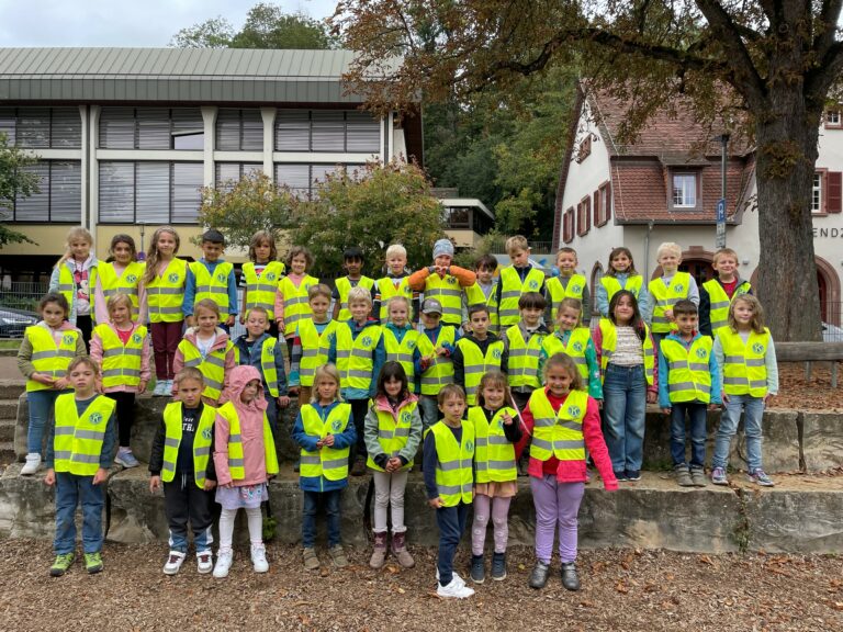 Das Bild zeigt die diesjährigen Erstklässlerinnen und Erstklässler in neonfarbenen Warnwesten aufgestellt in drei reihen auf dem Pausenhof.